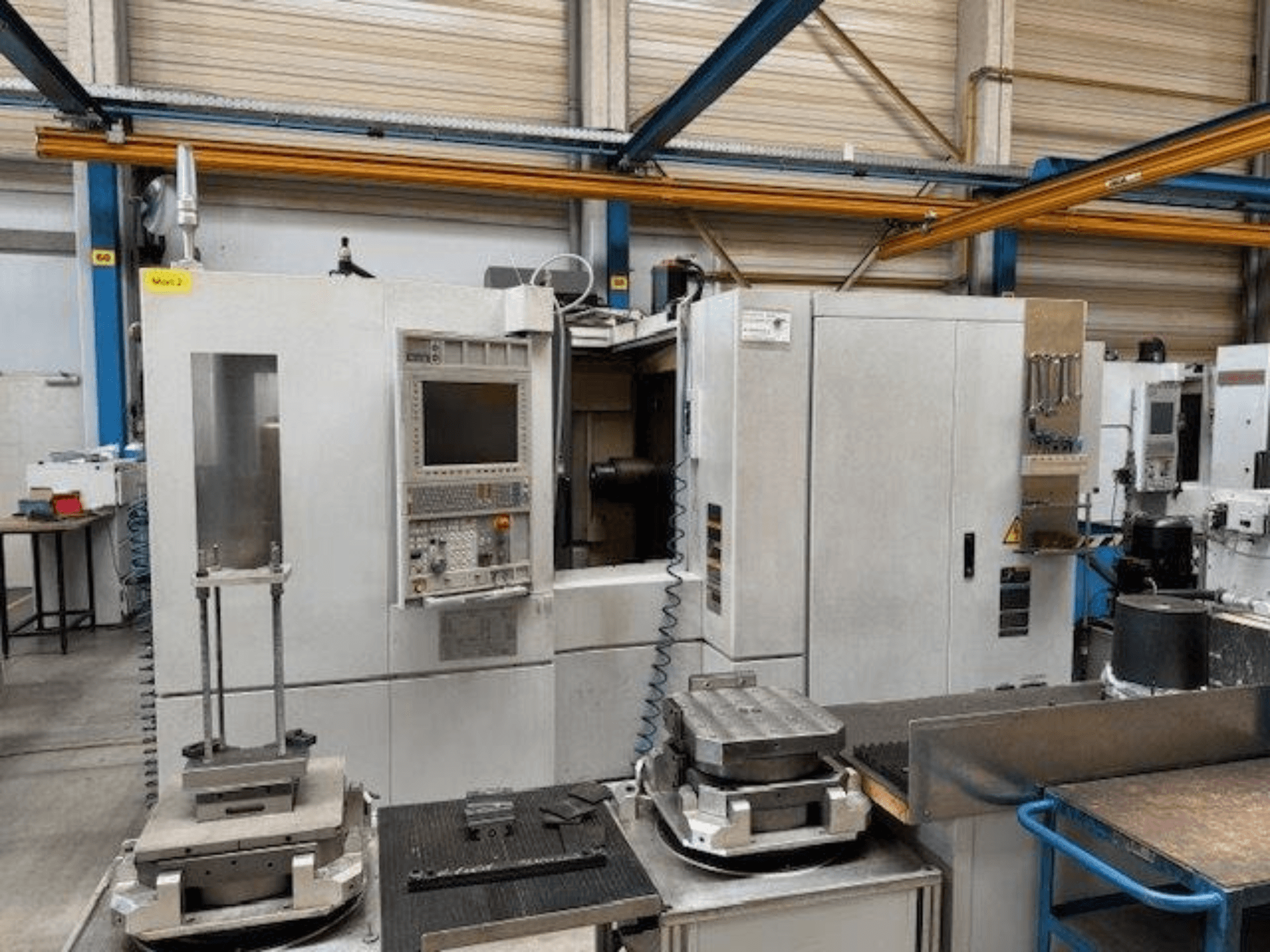 MORI SEIKI NH4000 DCG horizontālā apstrādes centra priekšējais skats ar vadības paneli un sagatavēm uz galda.