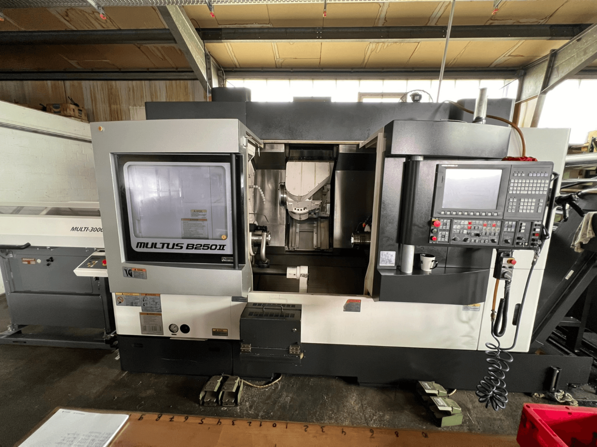Okuma Multus B250II MW virpošanas-frēzēšanas centrs, skats no priekšpuses, kurā redzams vadības panelis un apstrādes zonas detaļas.