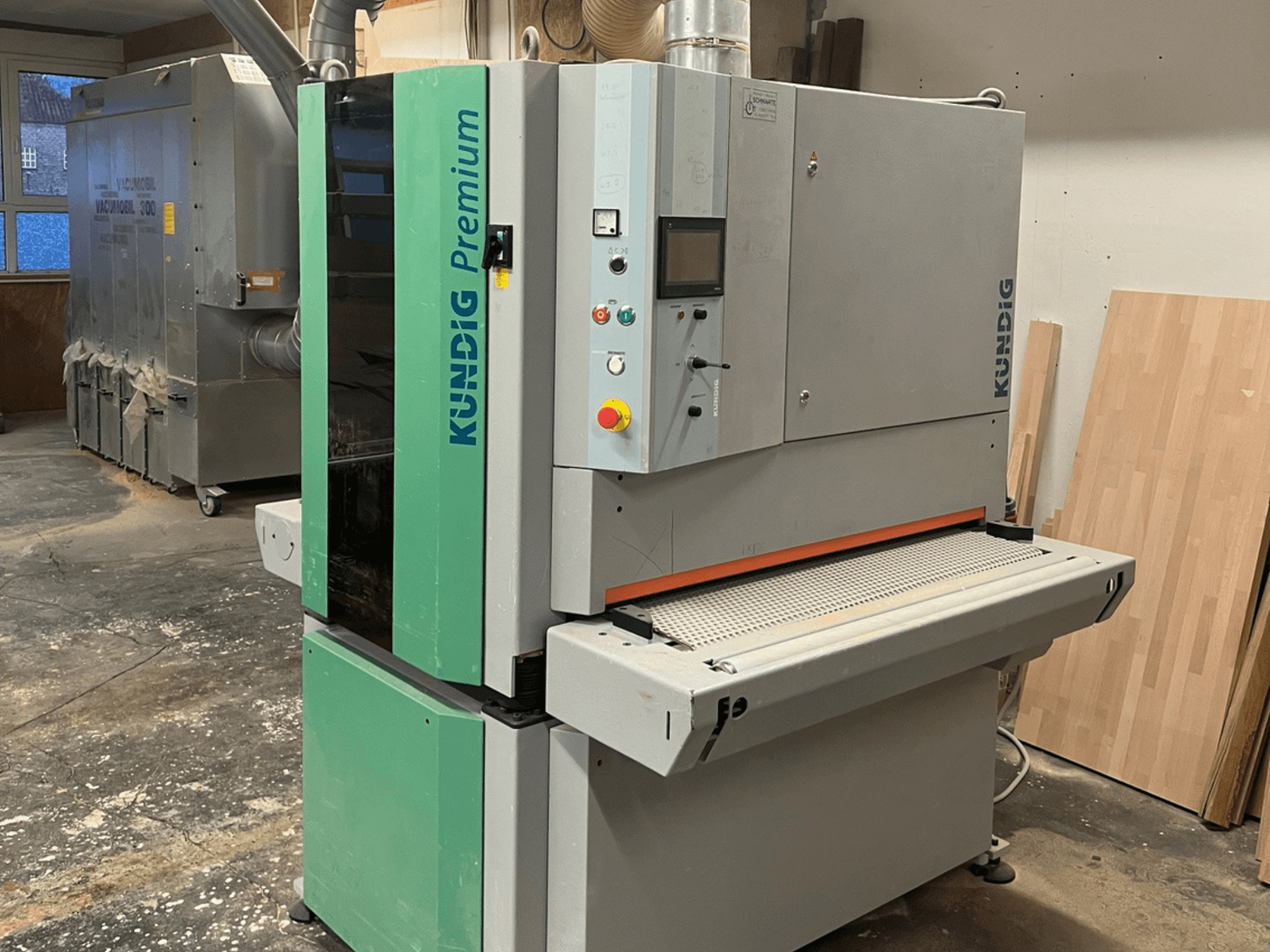 Kundig Premium-1 1100K lentes slīpmašīna pelēkā un zaļā krāsā, sānskatā ar redzamu vadības paneli un slīpēšanas lenti.