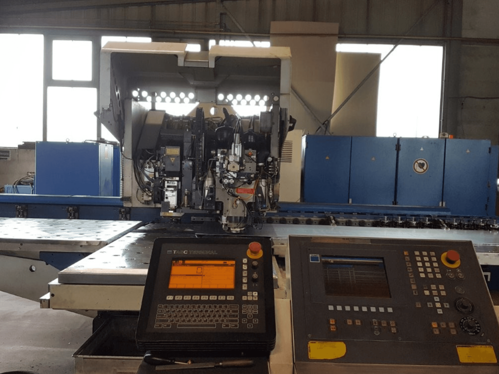 TRUMPF Trumatic 600L perforatora un lāzera kombinācija, priekšējais skats, kurā redzams vadības panelis un mašīnas detaļas darbnīcā.