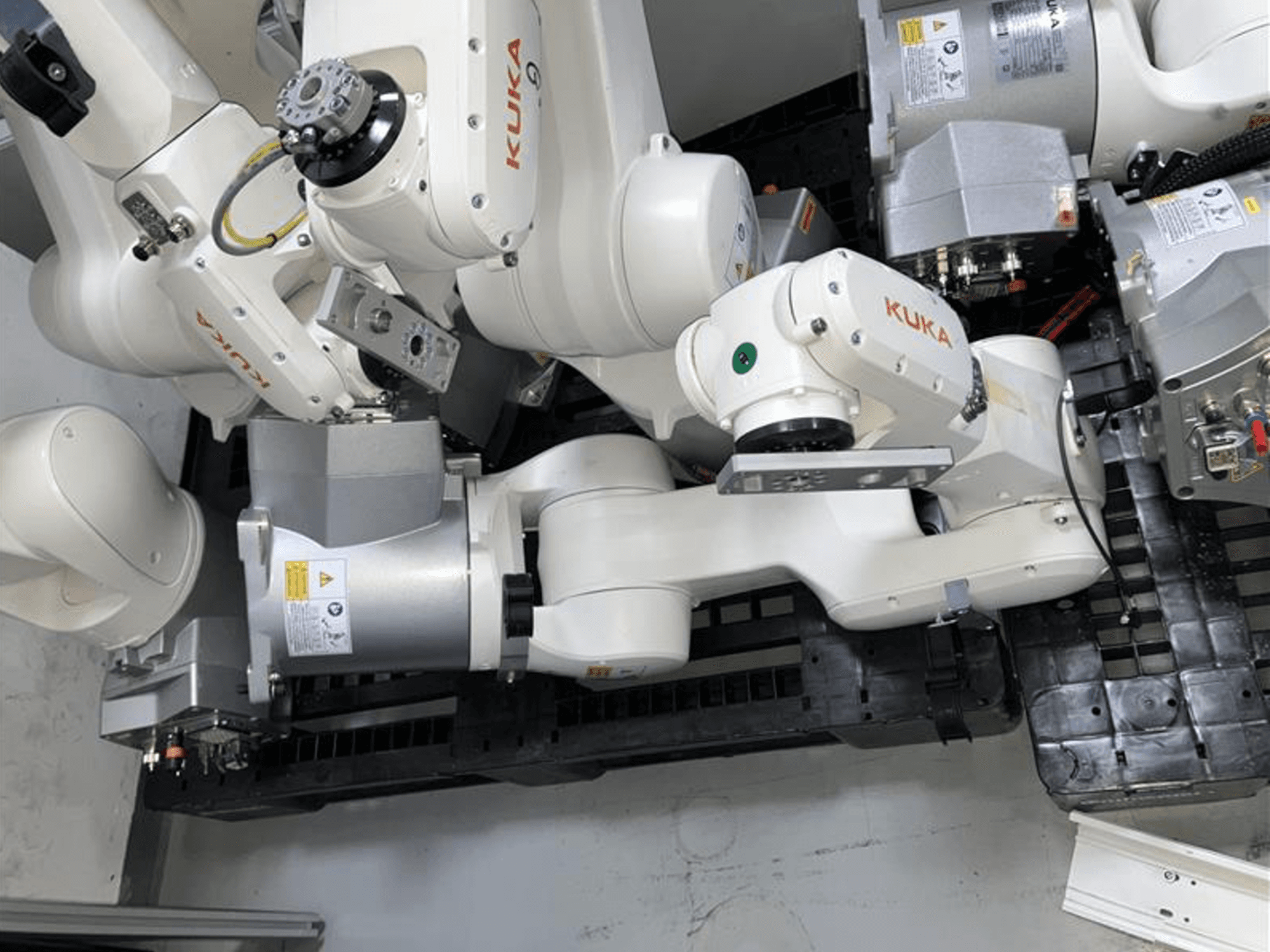 KUKA KR 10 R900-2 robota roka no augšas, demonstrējot šarnīrveida locītavas un piedziņas motorus rūpnieciskā vidē.