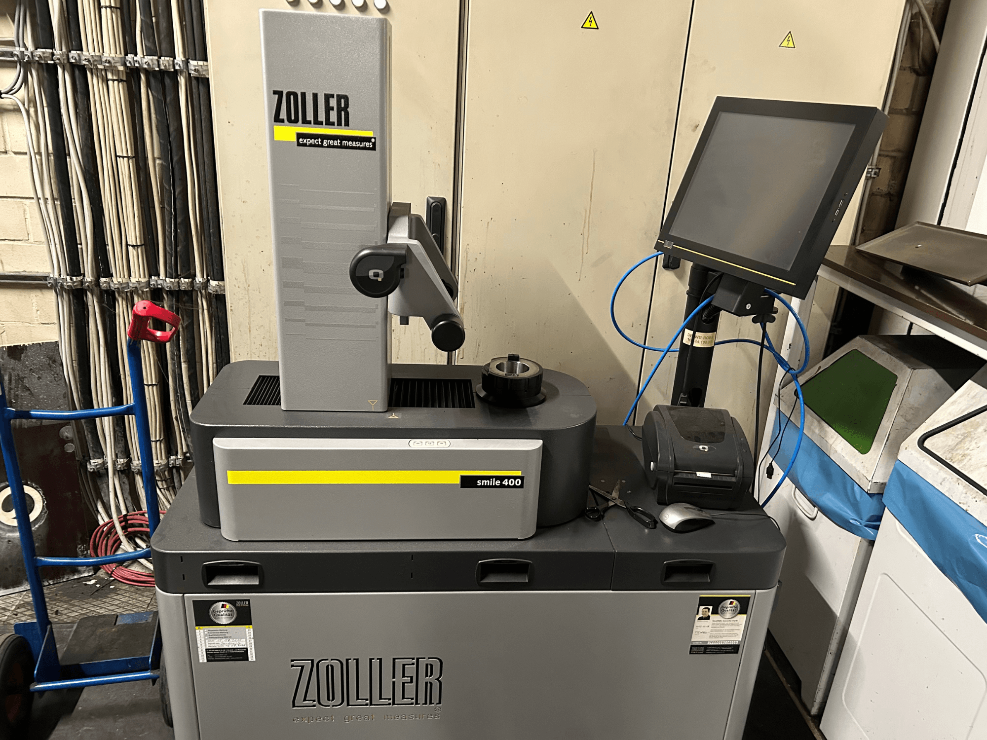 ZOLLER smile 400 mērīšanas iekārta pelēkā krāsā, skats no priekšpuses, ar skārienjūtīgo ekrānu, instrumentu turētāju un printeri uz darba virsmas.