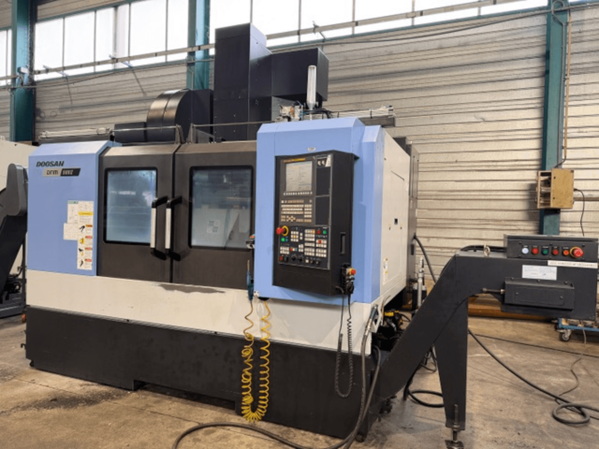 Doosan DNM 500II CNC frēzmašīna priekšpusē ar vadības paneli un instrumentu turētāju rūpnīcā.