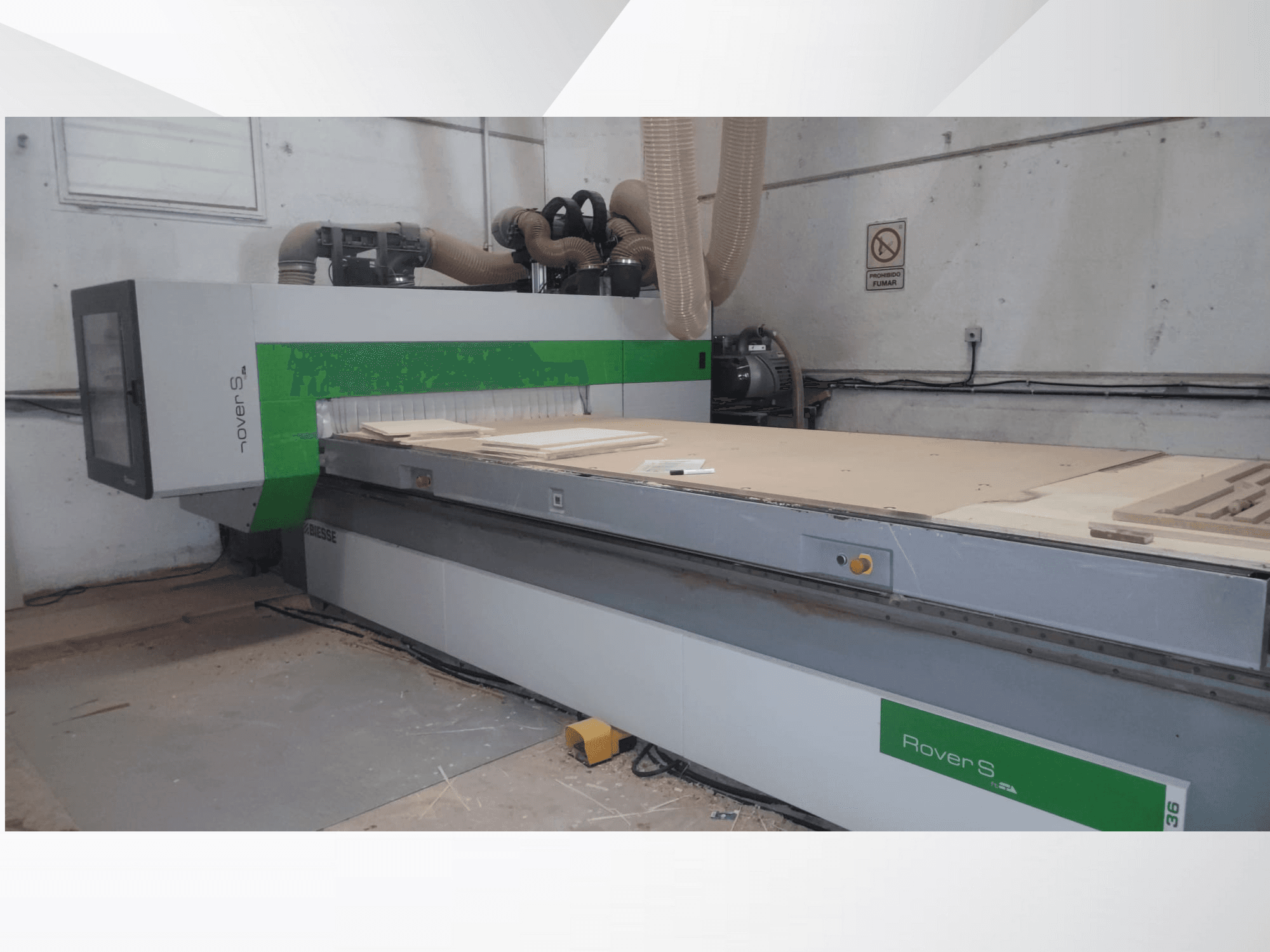 Biesse Rover S CNC mašīnas priekšējais skats ar lielu darba virsmu ar koka paneļiem un putekļu nosūces šļūtenēm.