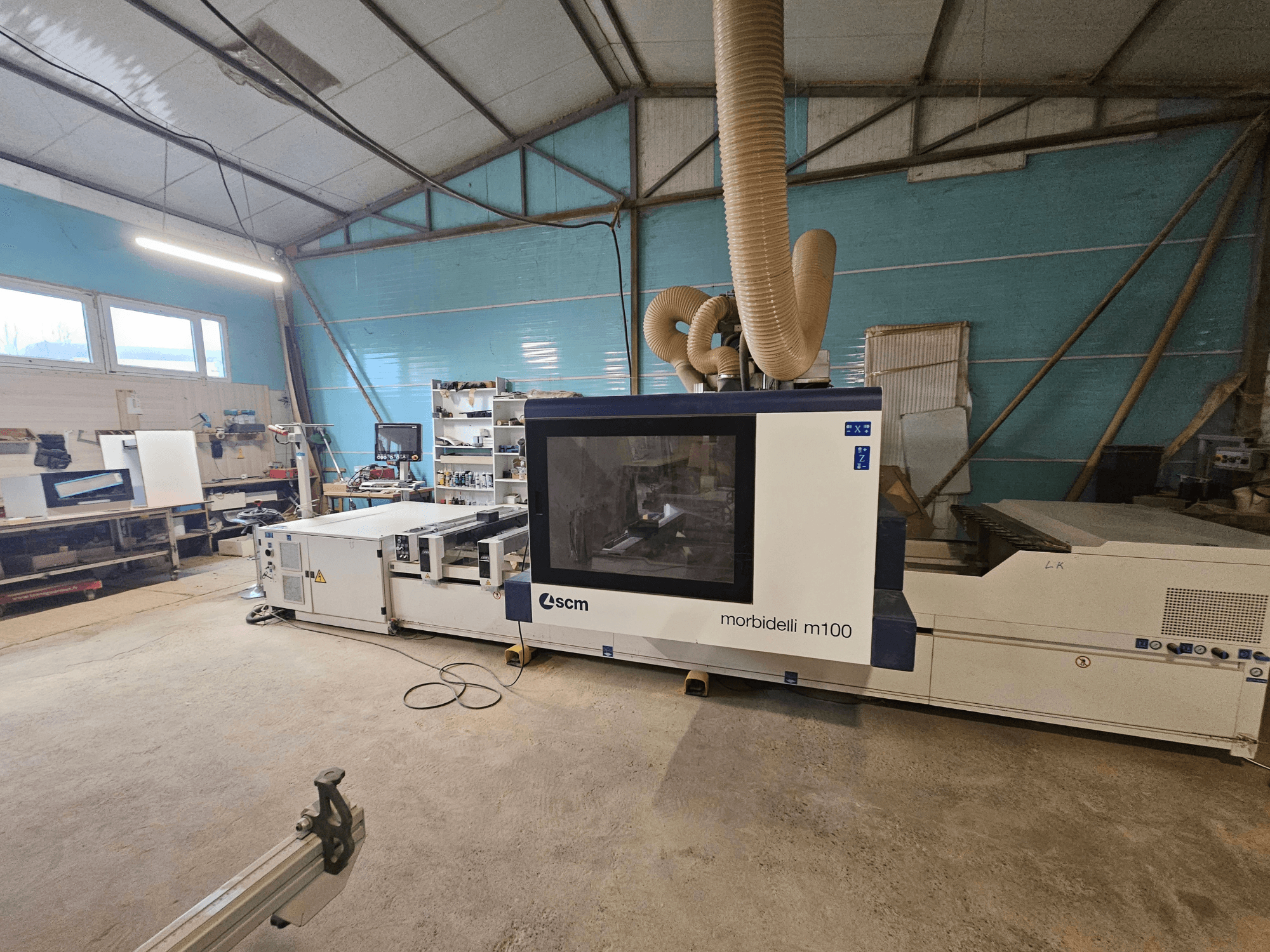 SCM Morbidelli M100 CNC mašīna darbnīcā, skats no priekšpuses, redzama putekļu nosūces sistēma un vadības panelis.