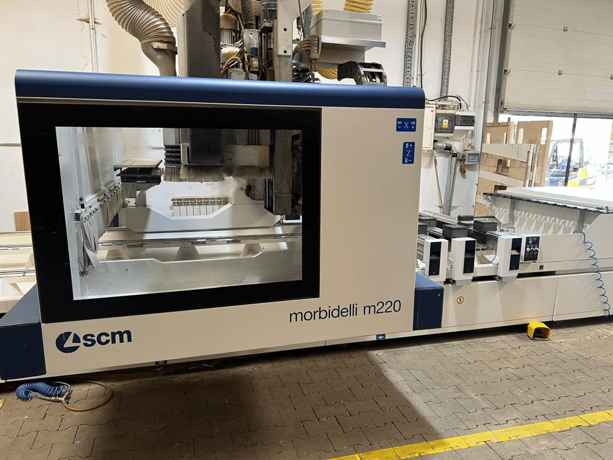 SCM Morbidelli M220 CNC apstrādes centra skats no priekšpuses, kurā redzams liels logs, vadības panelis un darba zona.