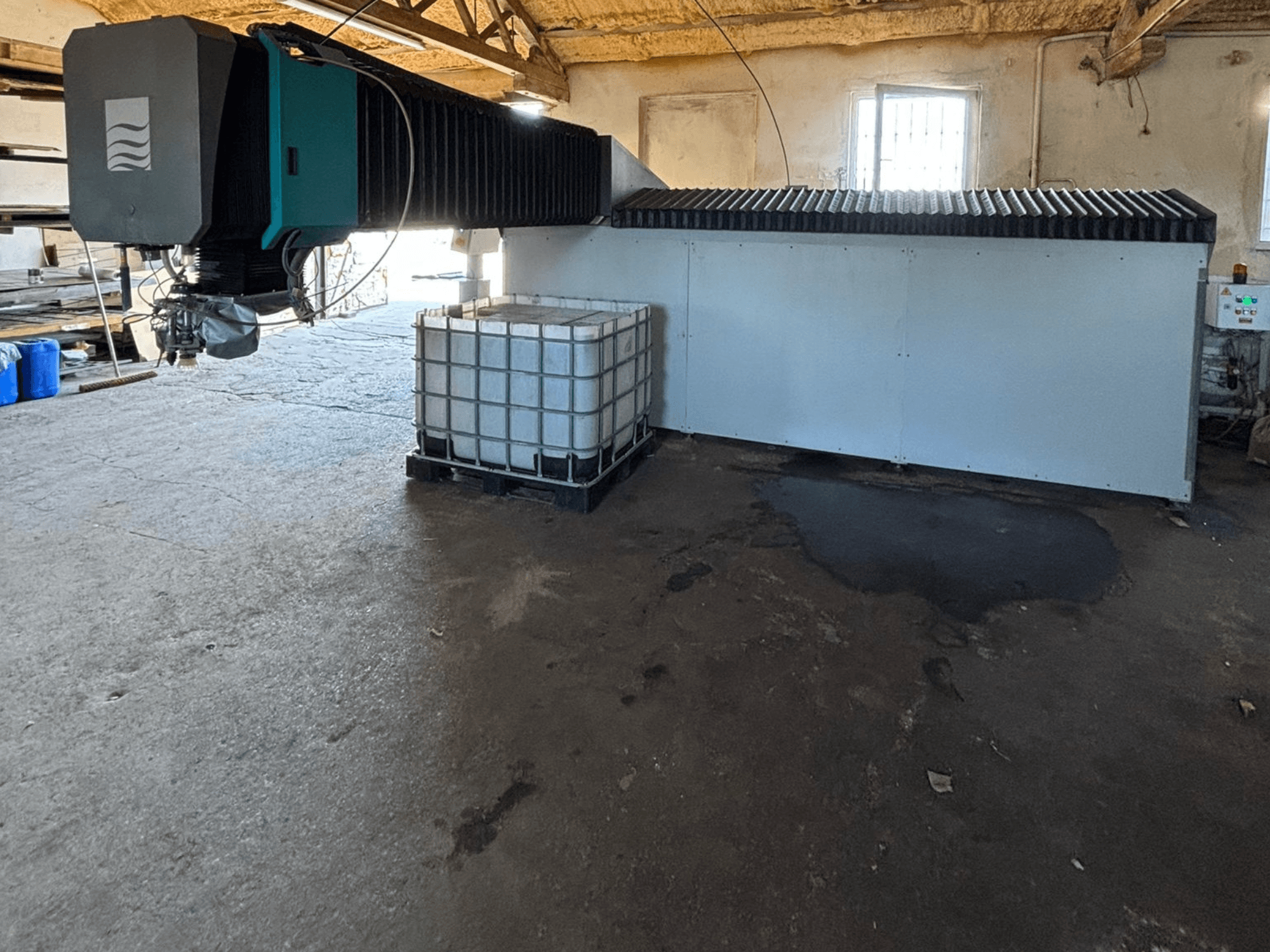 Rūpnieciskā ūdens strūklas mašīna darbnīcā, skats no sāniem, blakus redzama liela ūdens tvertne un vadības panelis.