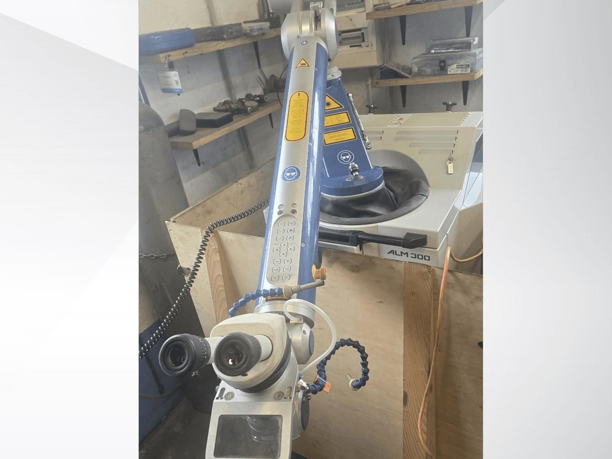Lāzera metināšanas iekārtas „ALPHA LASER ALM 300“ priekšskats, kurā redzama robota roka, optiskās lēcas un vadības panelis.