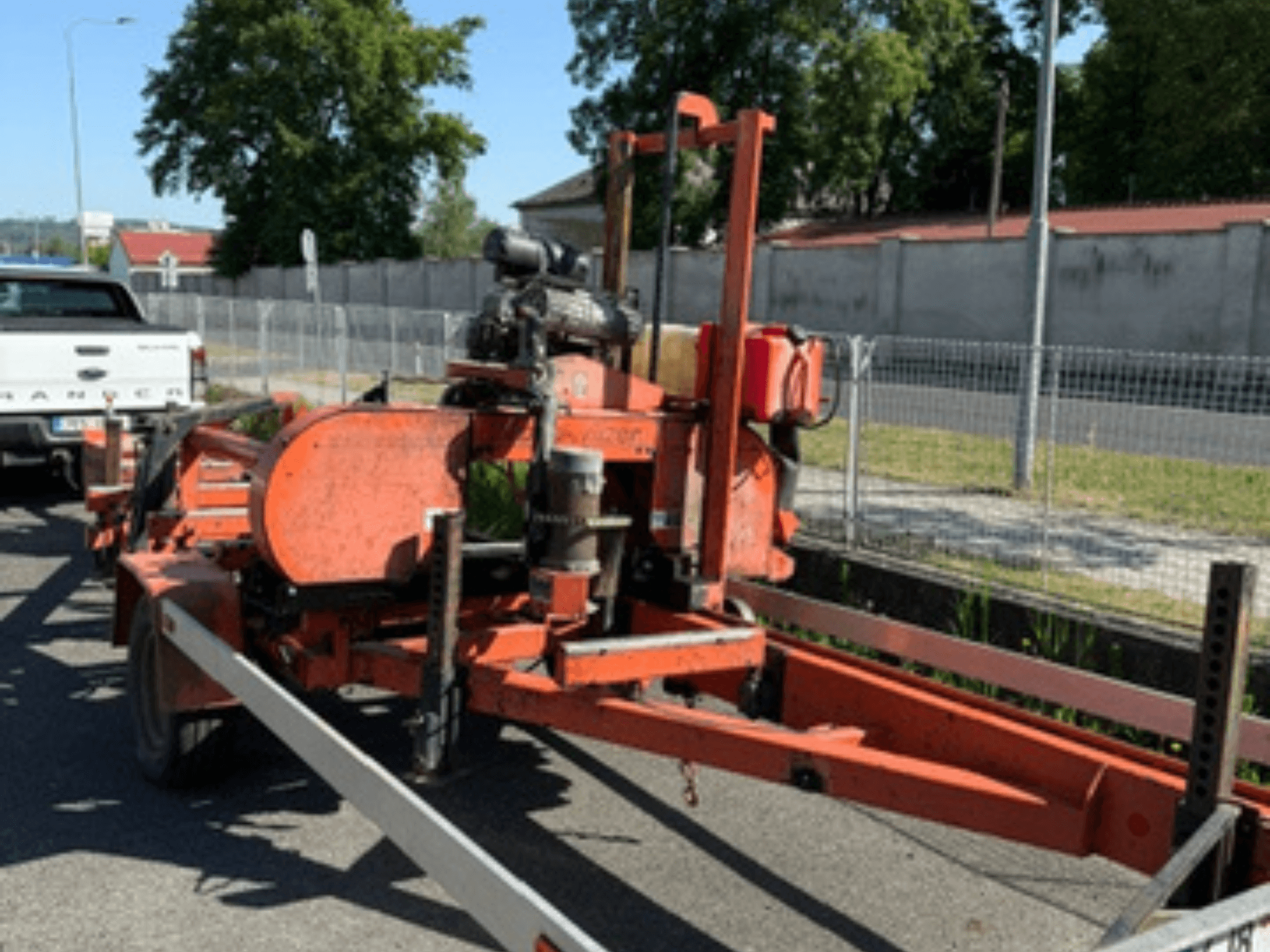 WOOD-MIZER LT40 koka lentes zāģis oranžā krāsā, sānskats uz piekabes ar redzamām riteņiem un dzinēja detaļām.
