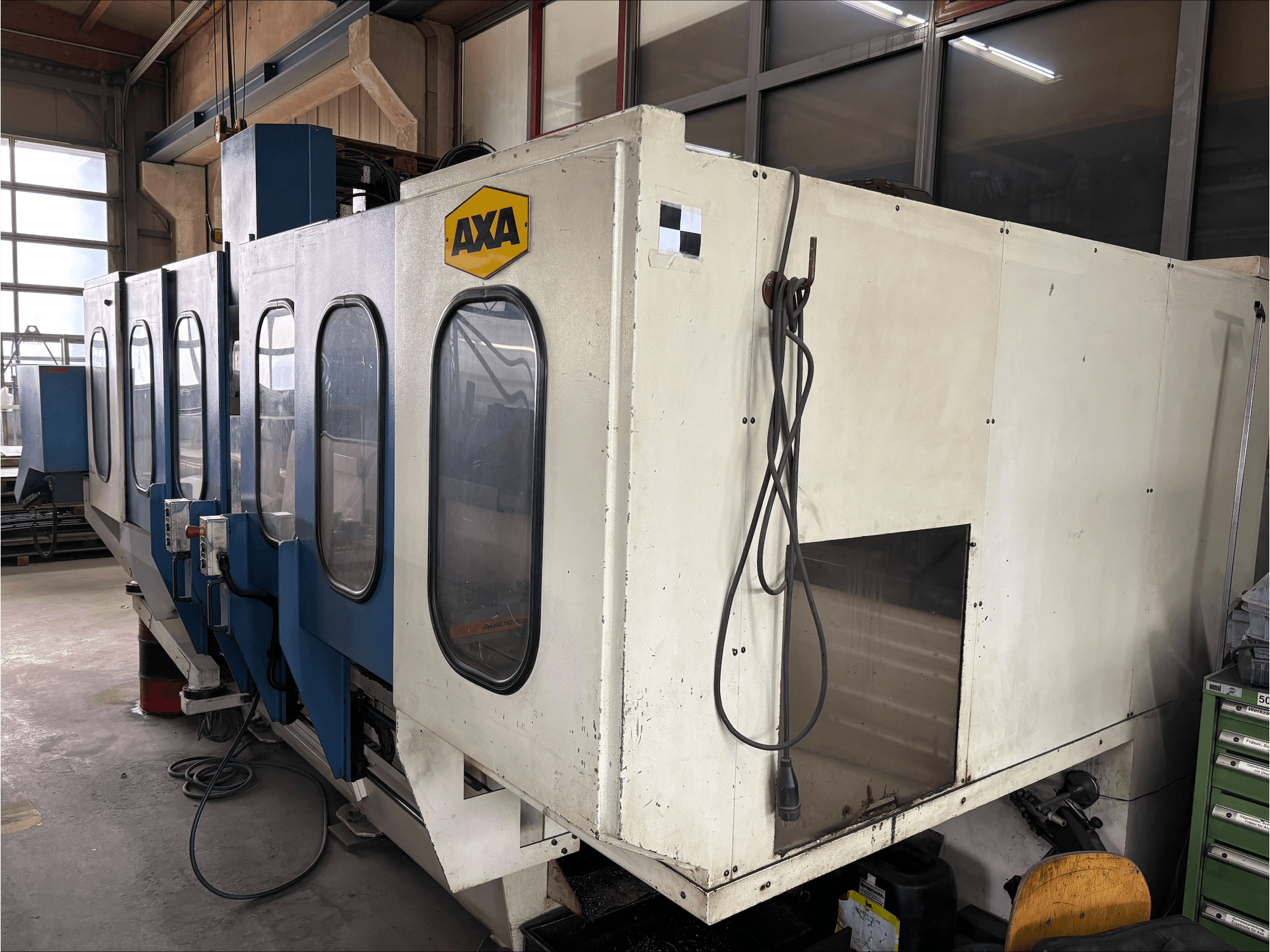 AXA VSC-1-M/C vertikālais apstrādes centrs, skats no priekšpuses, ar lielu baltu korpusu un zilu vadības paneli.