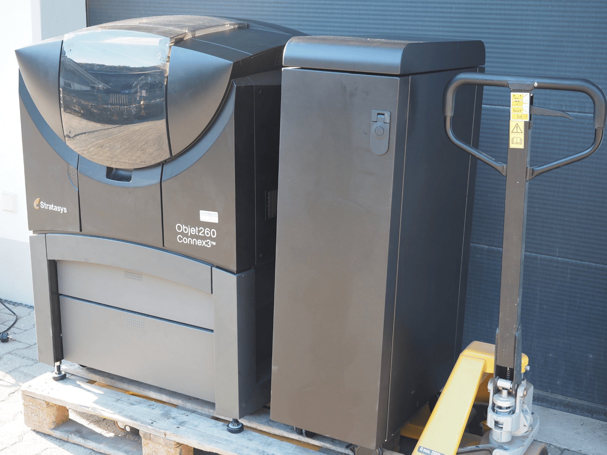 Stratasys Objet260 Connex3 plastmasas 3D printeris, skats no sāniem, ar kompaktu dizainu, vadības paneli un pievienotu materiālu tvertni.