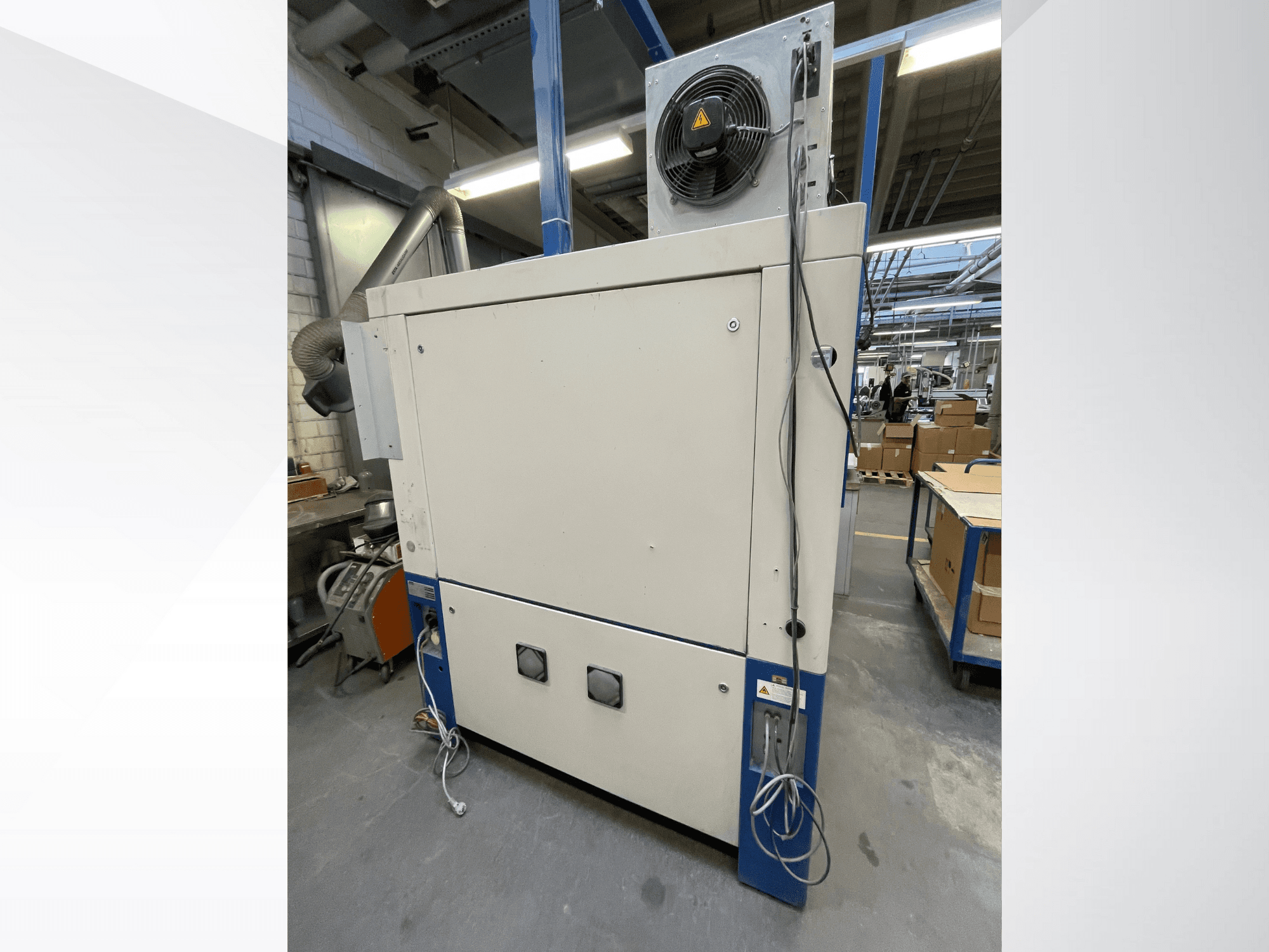 Rūpnieciskā žāvēšanas iekārta ar ventilatoru, skats no sāniem; aprīkota ar ventilāciju un vairākiem elektrības savienojumiem. Zīmols/modelis nav redzams.