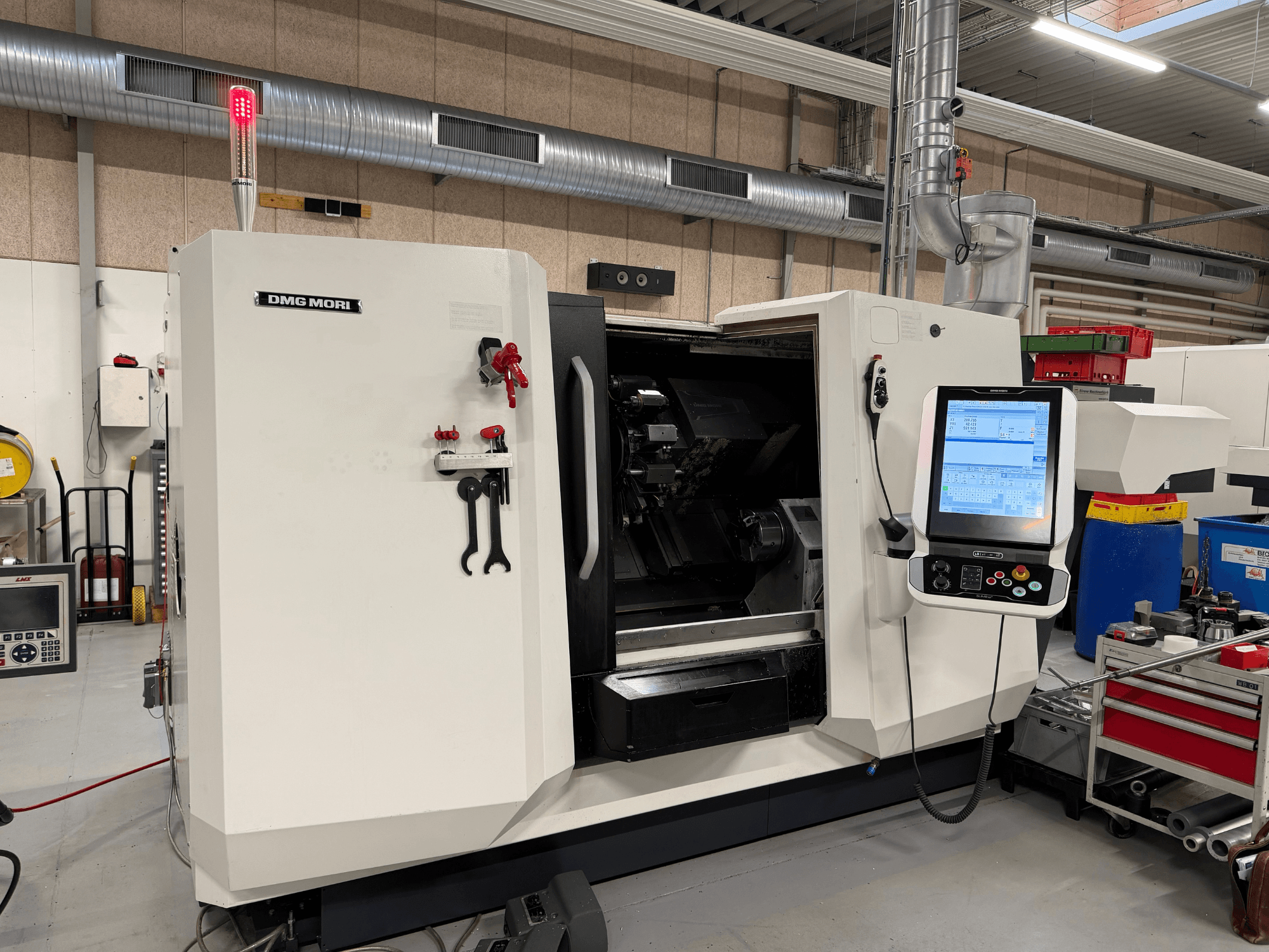 DMG MORI CLX 450 V6 horizontālā virpošanas mašīna, skats no priekšpuses, kurā redzams vadības panelis, avārijas apstādināšanas poga un drošības gaisma.