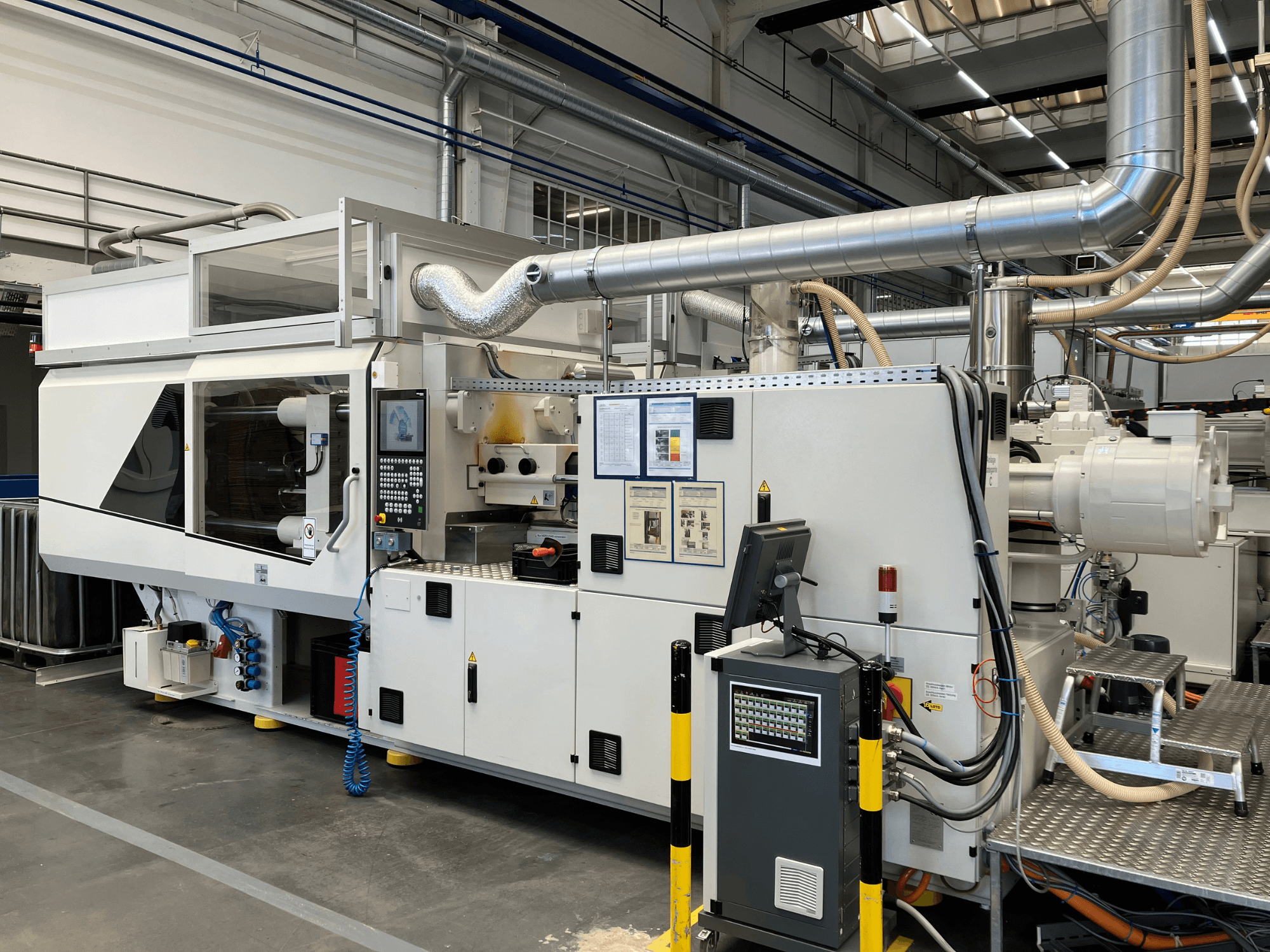 Priekšējais skats uz rūpniecisku mašīnu ar vadības paneli, caurulēm un displeja ekrāniem, ar gludu baltu dizainu un tehniskām detaļām.