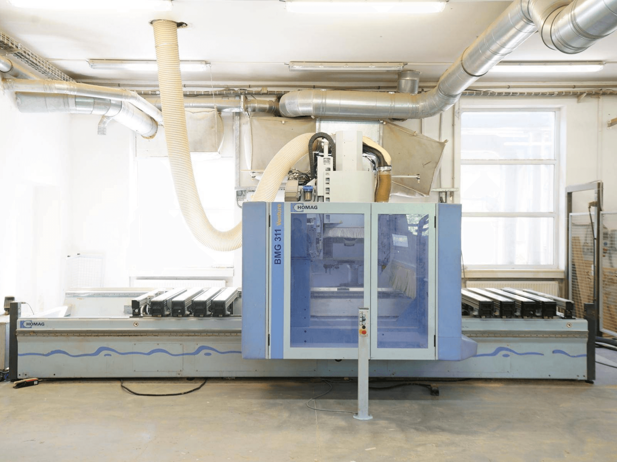CNC kokapstrādes centrs HOMAG V BMG 311/42/F/K, skats no priekšpuses, ar lielu darba galdu un putekļu nosūces sistēmu.