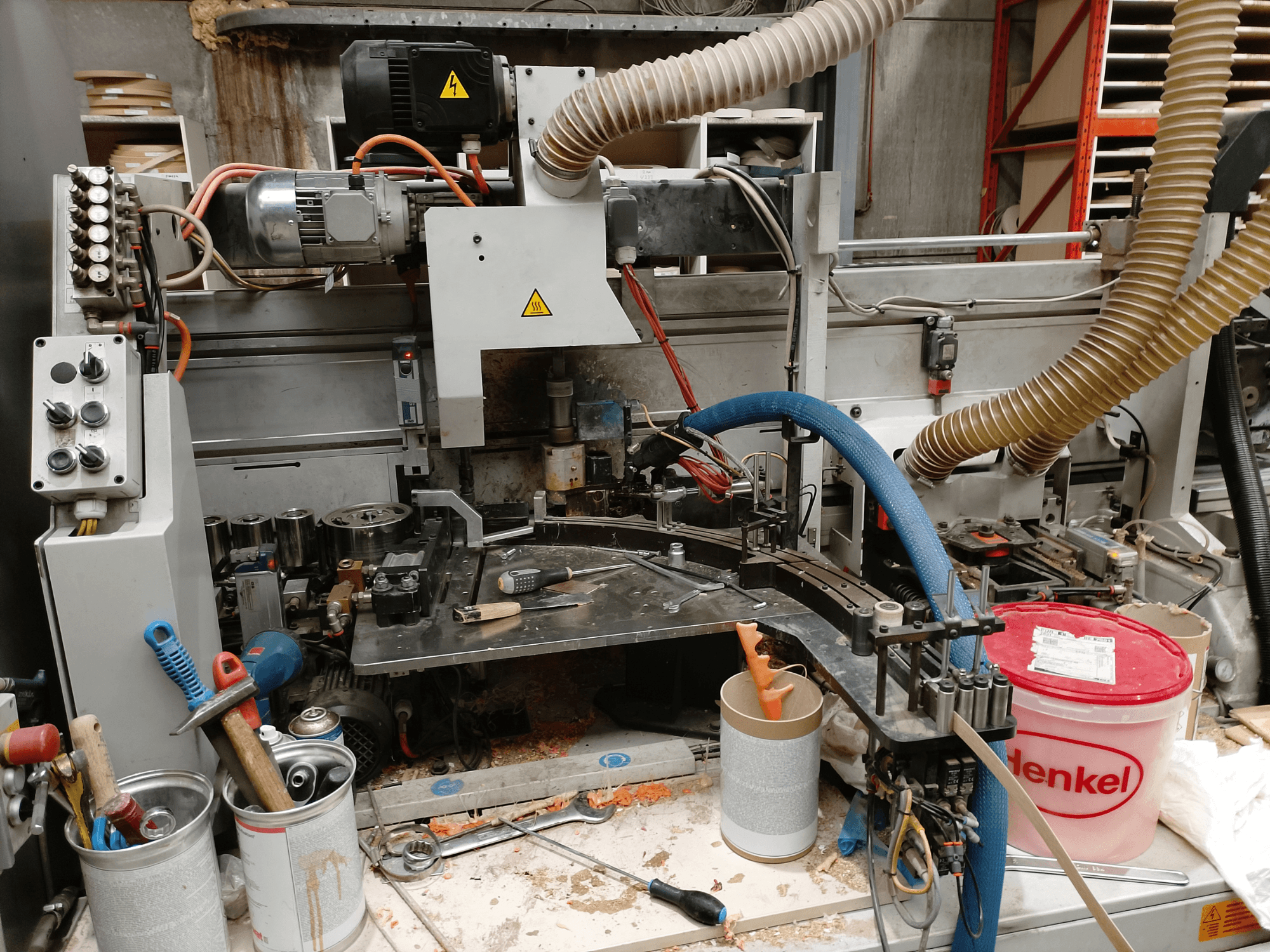 BIESSE Edge Stram B1 malu apstrādes iekārta priekšpusē, kurā redzamas iekārtas, šļūtenes un darba rīki starp koka skaidām.