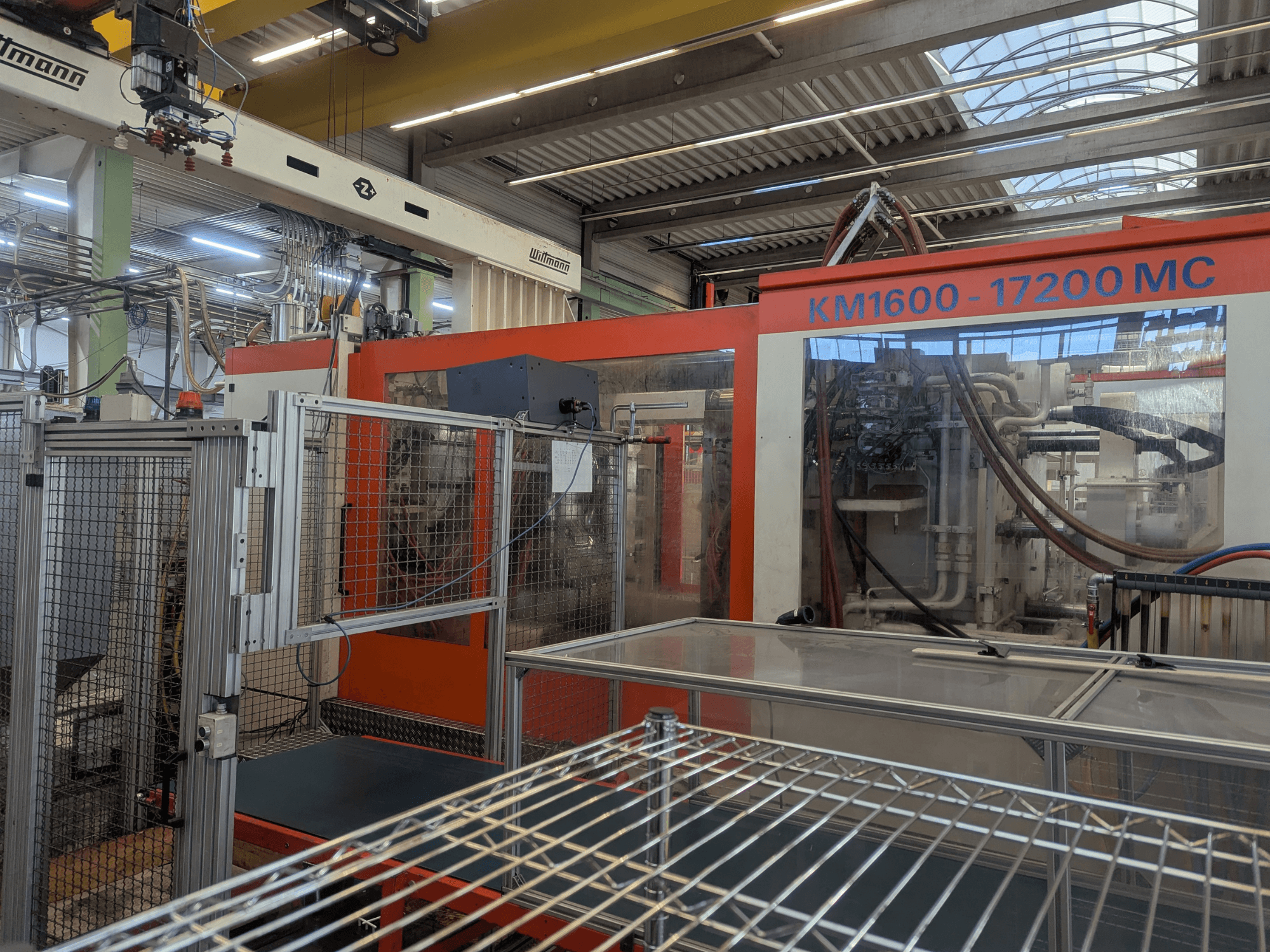 Hidrauliskā iesmidzināšanas iekārta Krauss Maffei KM 1600-17200MC, priekšējais skats ar redzamu vadības paneli un hidrauliskajām līnijām.