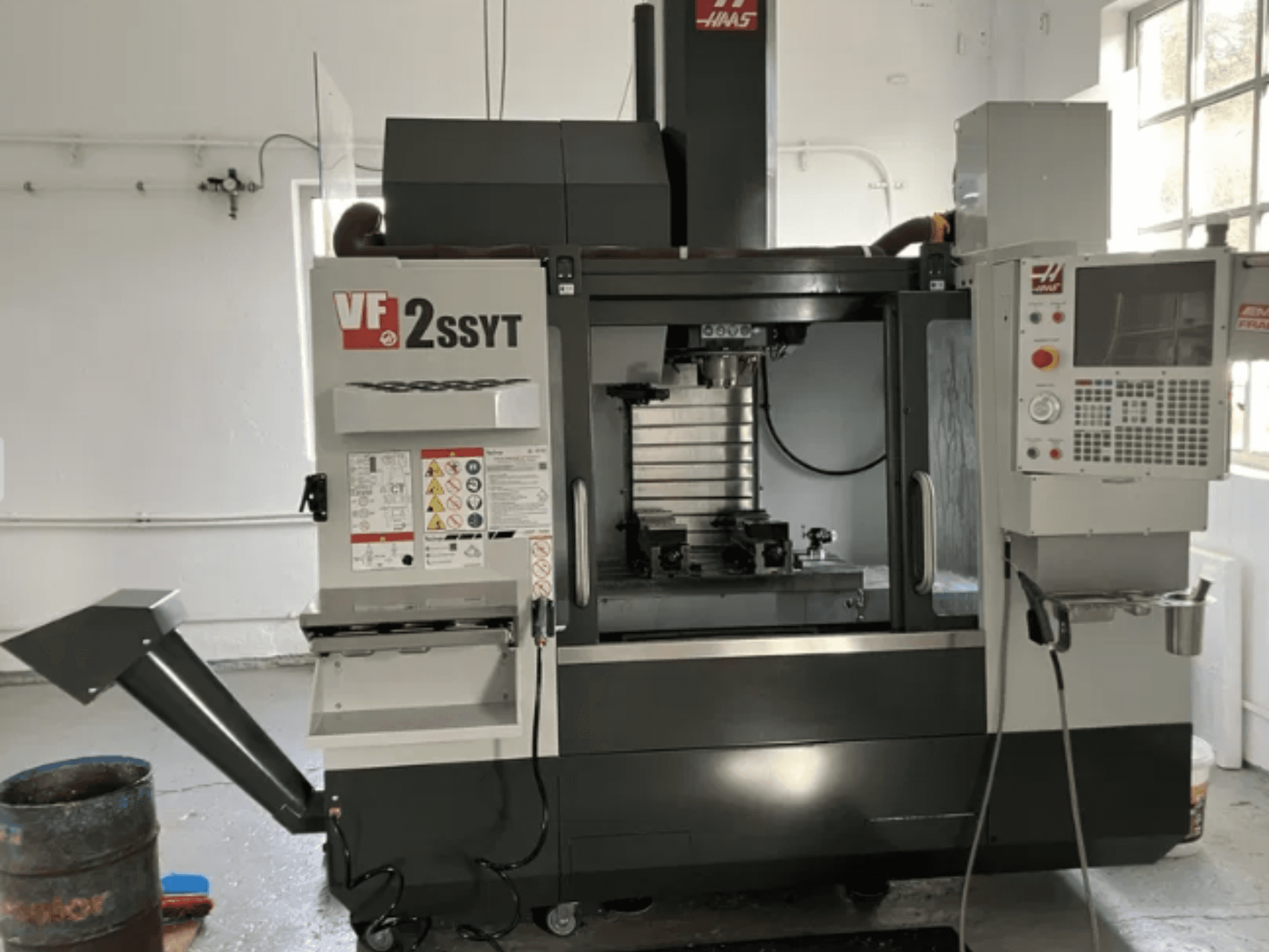 Haas VF-2SSYT CNC frēze, skats no priekšpuses, ar vadības paneli, instrumentu turētāju un dzesēšanas sistēmu metāla apstrādei.