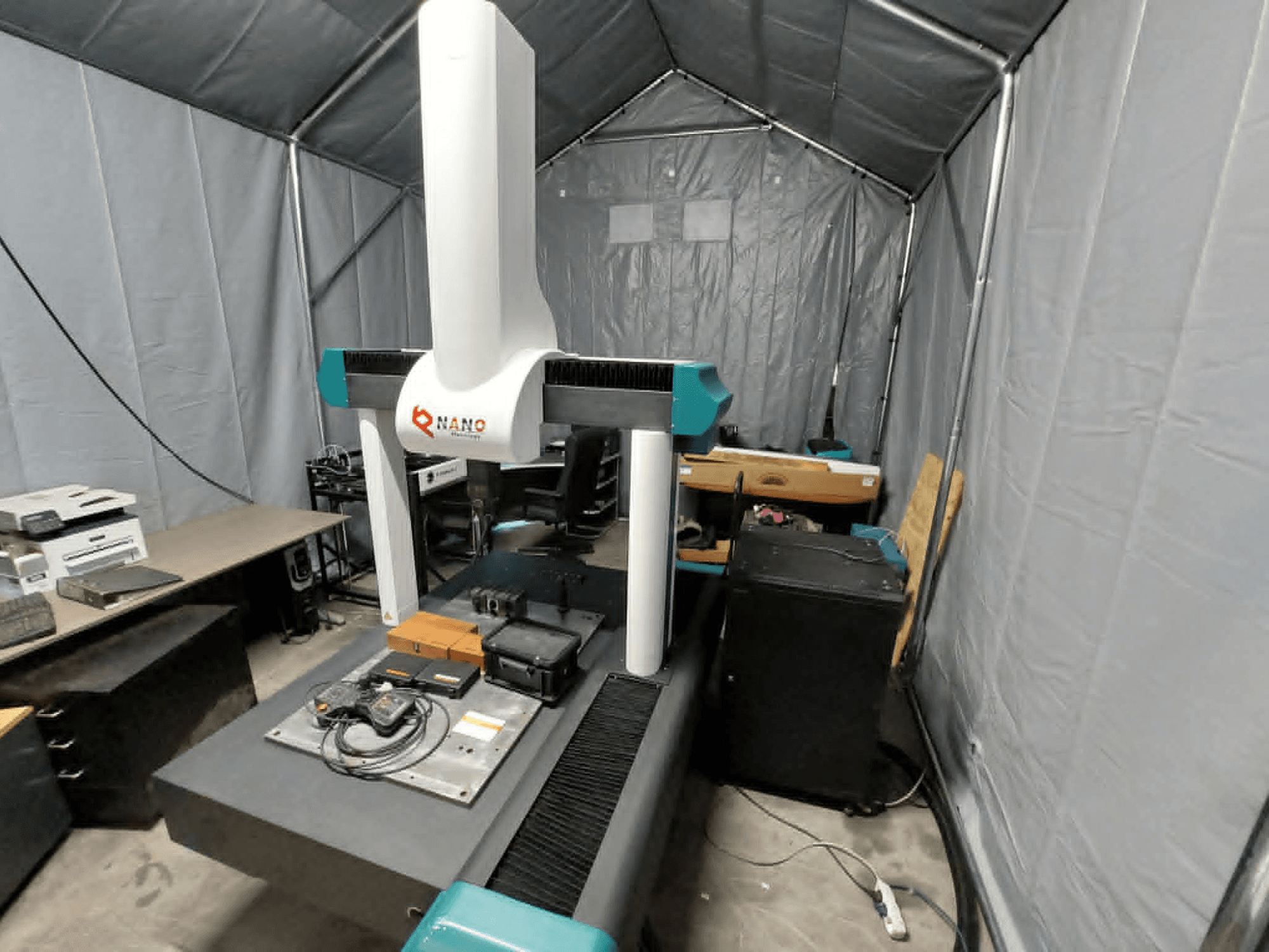 NANO METROLOGY Micr 7106 CMM teltī; priekšējais skats, kurā redzama mašīnas roka un mērīšanas platforma ar piederumiem.