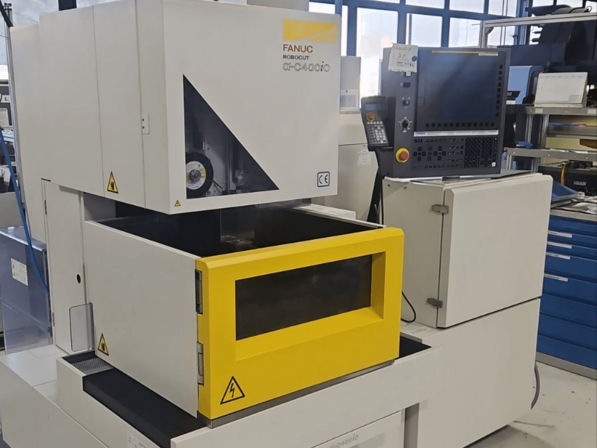 FANUC Robocut alpha-C400iC dziļumgriešanas elektroerozijas mašīna, skats no priekšpuses, ar dzeltenu detaļu kameru un vadības paneli.
