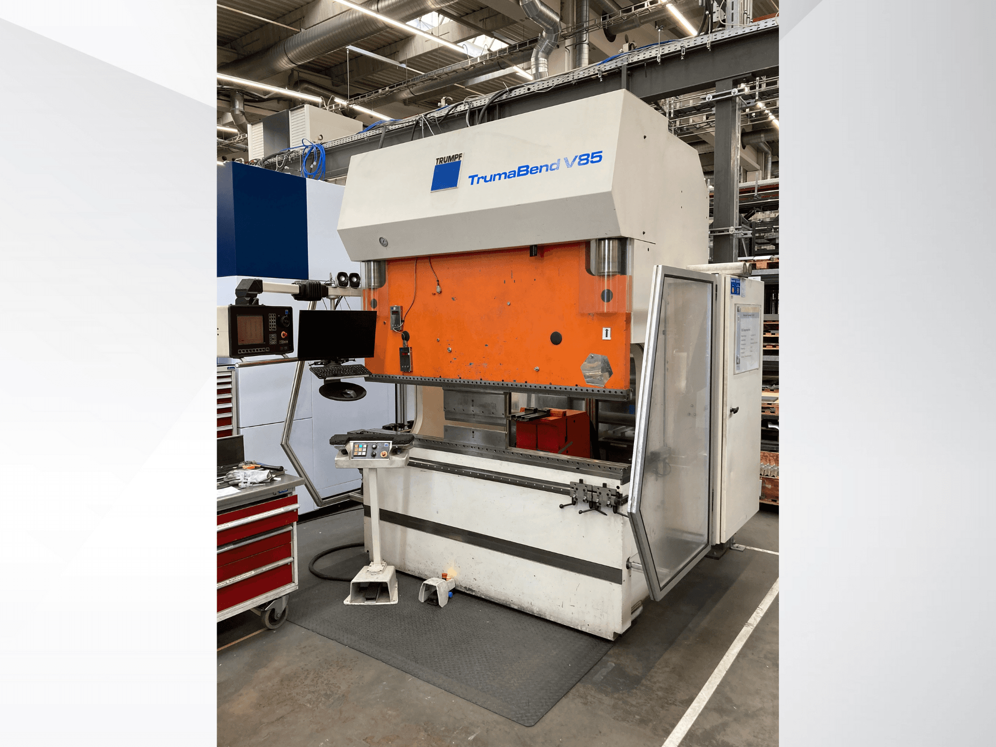 TruMatic V85 liekšanas iekārta rūpnīcā, ar oranžu priekšējo paneli, vadības ekrānu un atvērtām sānu durvīm, skats no malas.