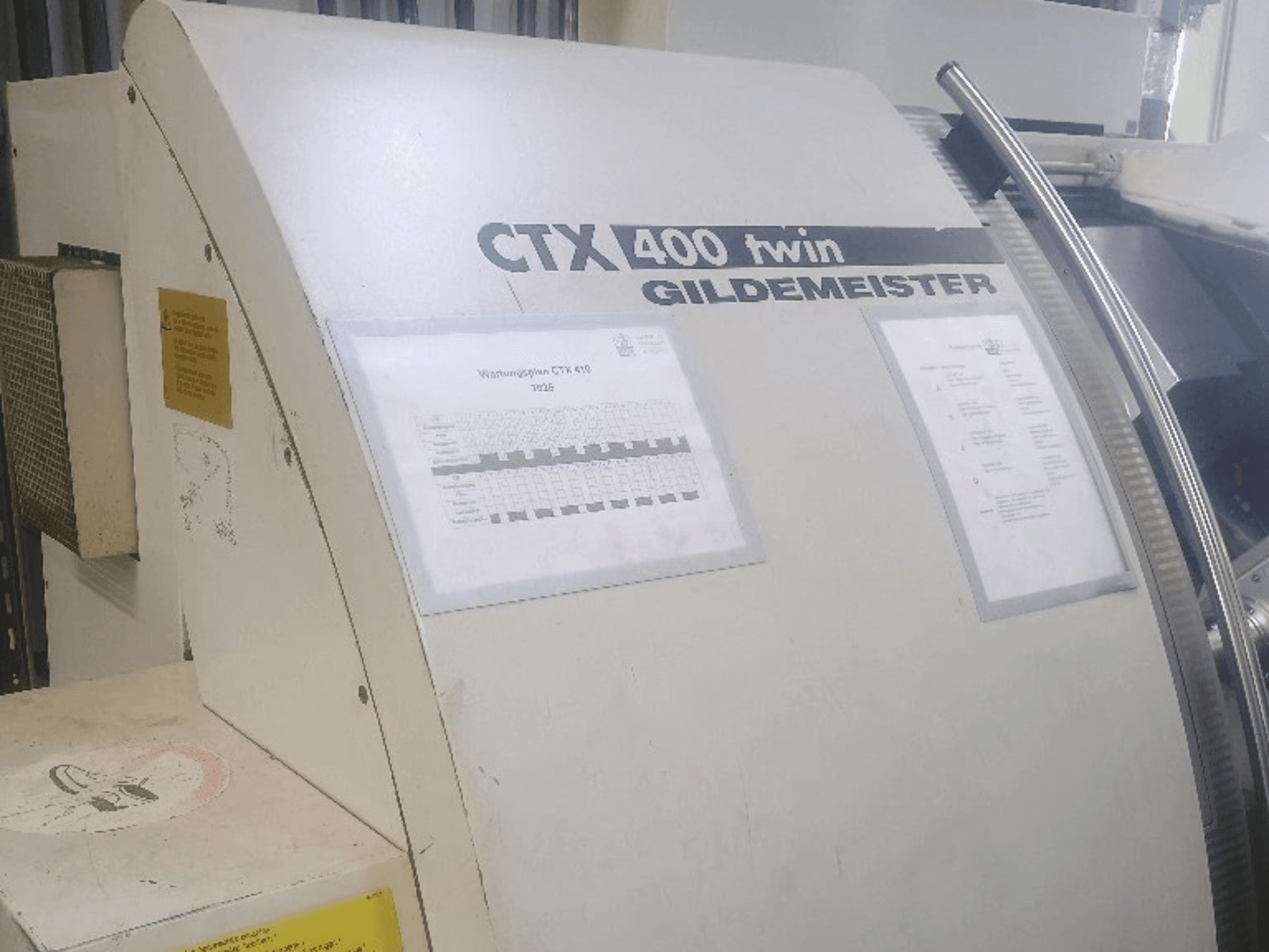 Gildemeister CTX 400 divkāršā horizontālā virpošanas mašīna, skats no priekšpuses, kurā redzamas vadības paneļi un tehniskā dokumentācija.