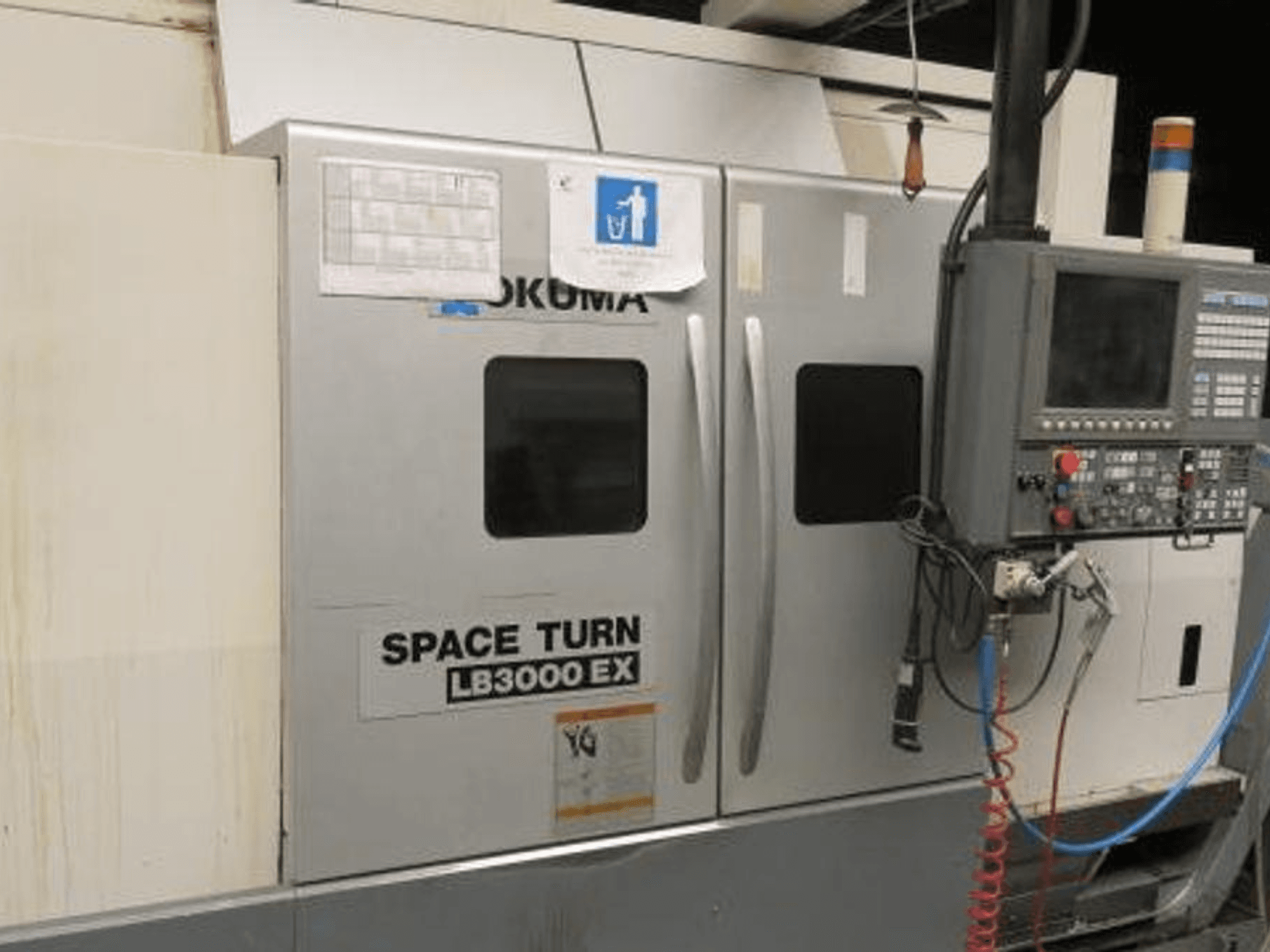 Okuma Space Turn LB3000 EX CNC virpa, skats no sāniem, ar vadības paneli, divām durvīm un redzamiem vadiem.